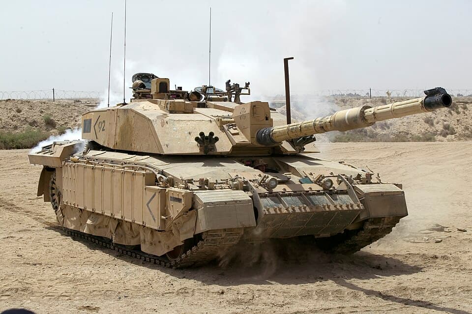 Front three-quarter photograph of a Challenger 2 in desert camouflage, with its turret, gun, tracks and side armour visible.